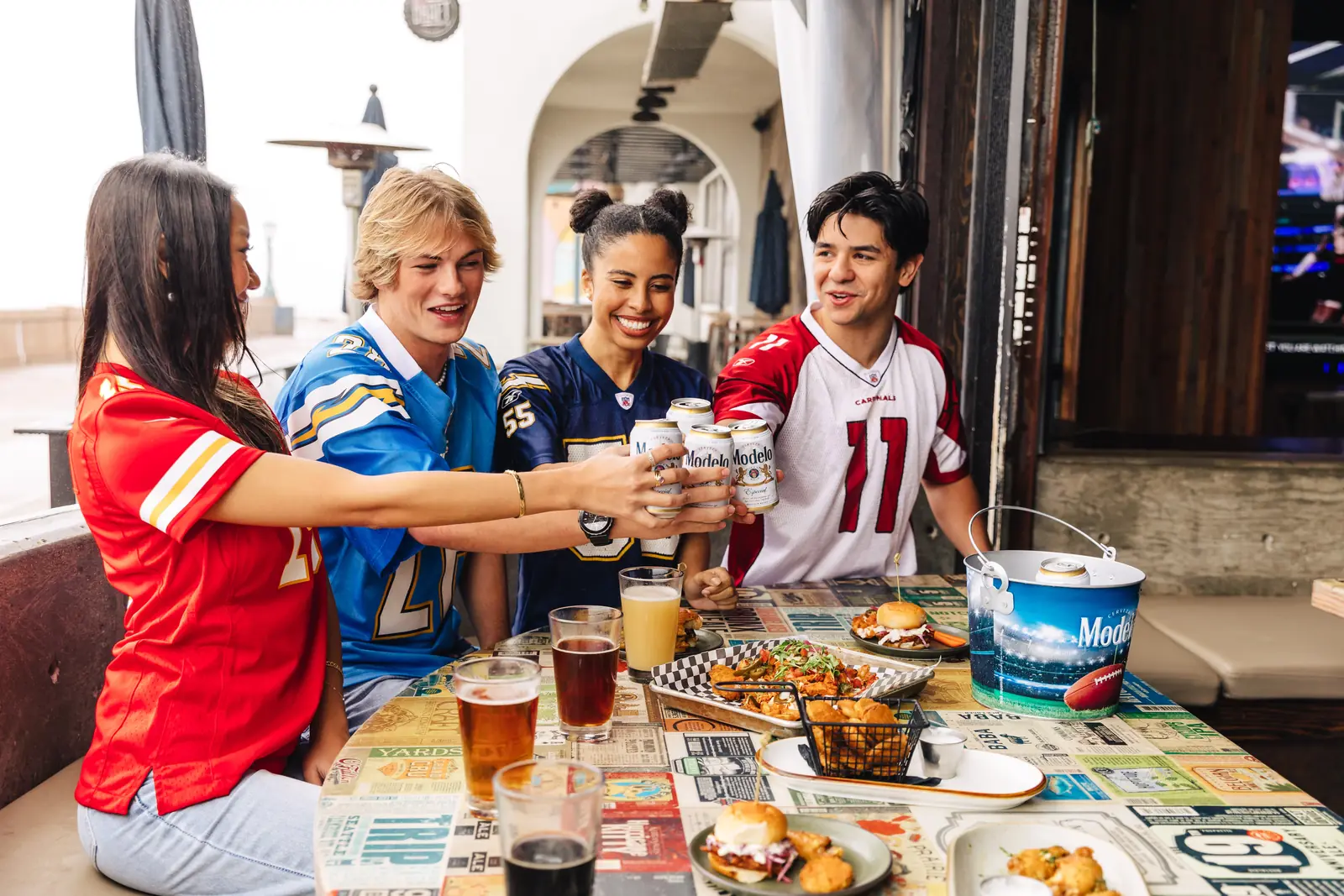 Four friends in football jerseys raising a toast over shared plates at a sports bar table